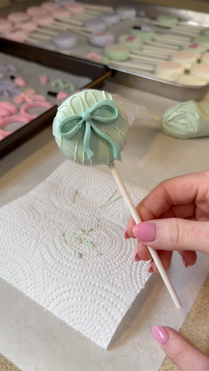 Light green cake pop with a frosting bow held by a hand.