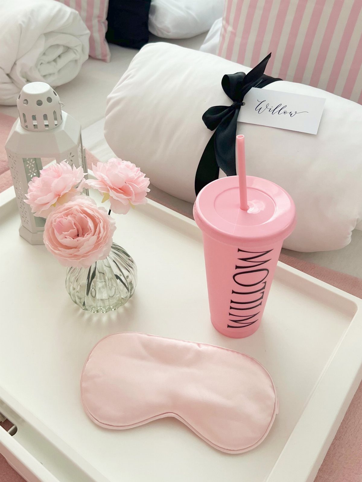 Pink sleep mask, tumbler, and flowers on a tray next to rolled blankets.