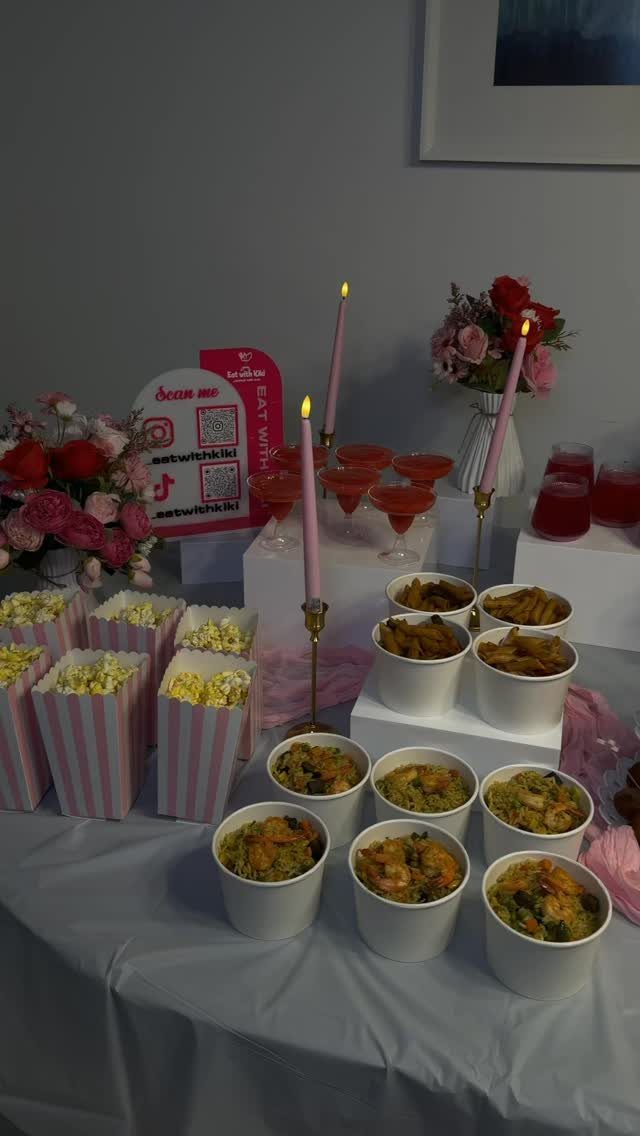 Party food spread with popcorn, snacks, red cocktails, and pink candles on a table.