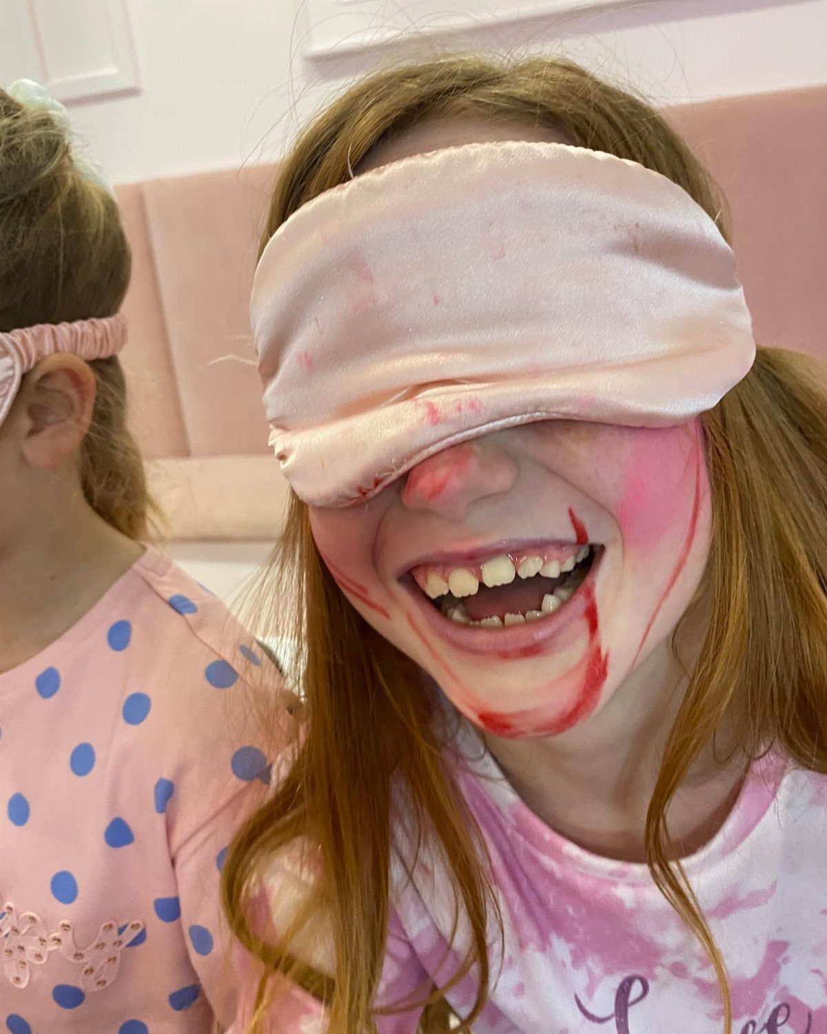 Girl wearing a pink sleep mask with messy red makeup smeared on her face.