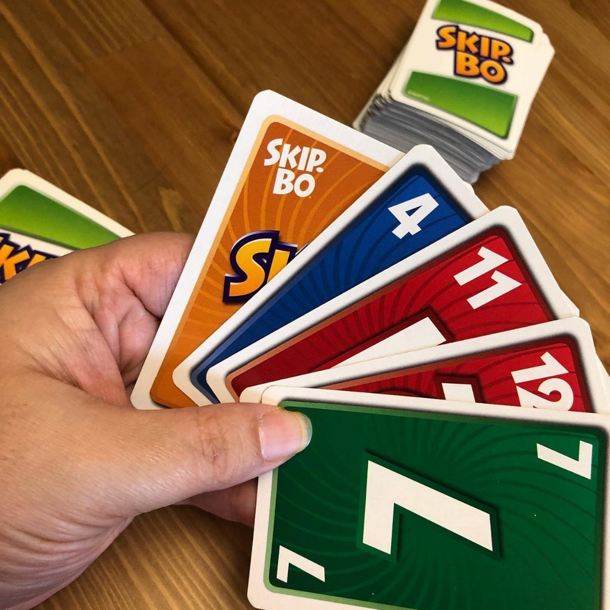 Hand holding a fan of colorful Skip-Bo cards on a wooden table.