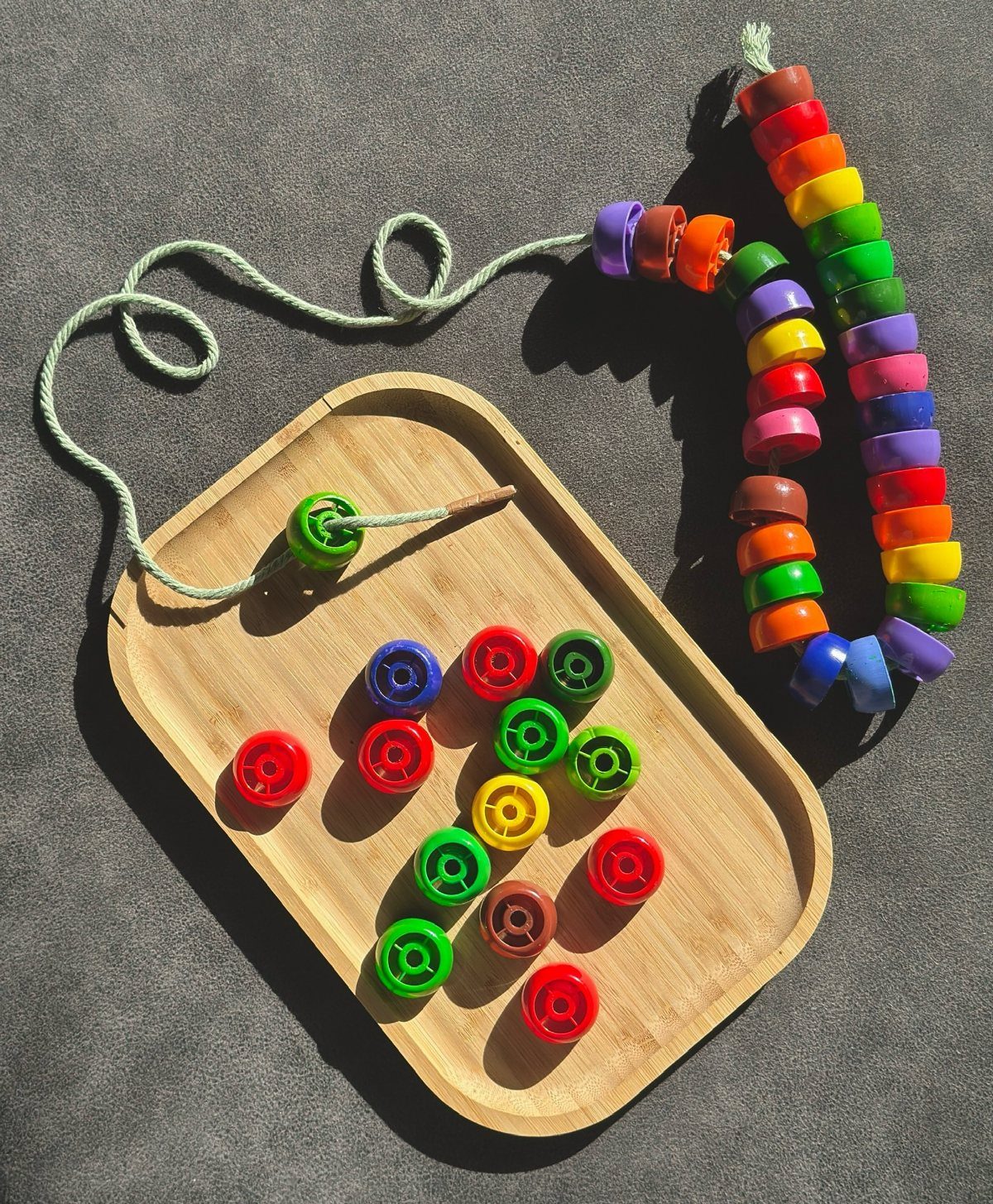 Colorful plastic beads on a wooden tray and a strung bead necklace.