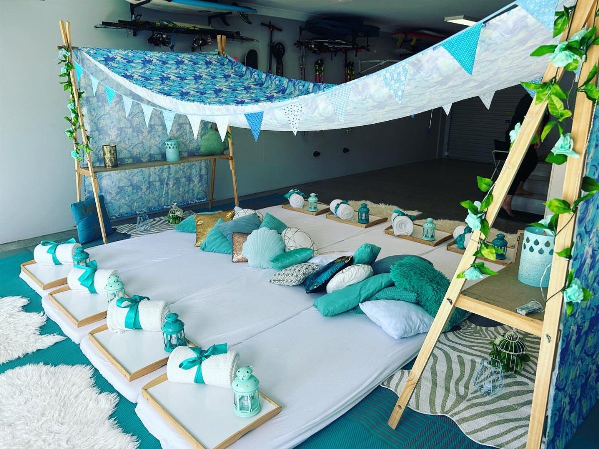 Cozy slumber party setup with white mattresses, teal pillows, and a blue canopy.