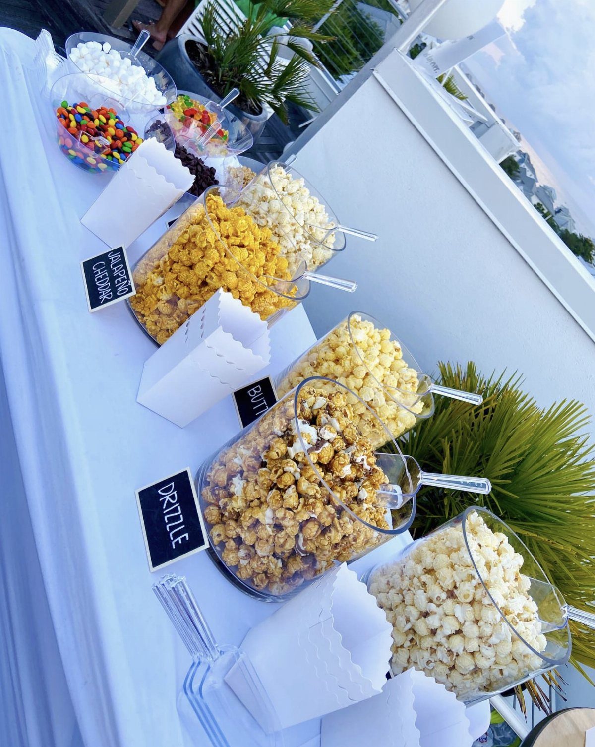 Popcorn bar with various flavored popcorns, candies, and marshmallows in clear containers.