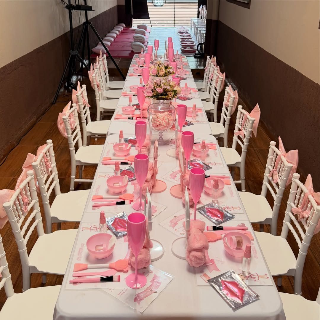 Long white table set with pink spa supplies, bowls, and facial masks for guests.