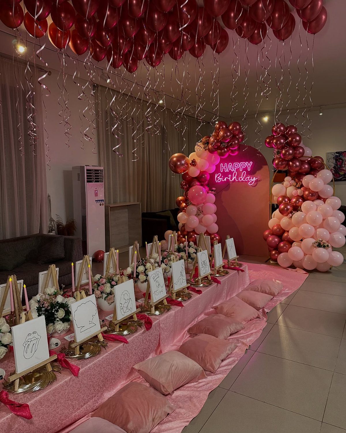 Pink birthday party setup with a long decorated table and balloon arch.