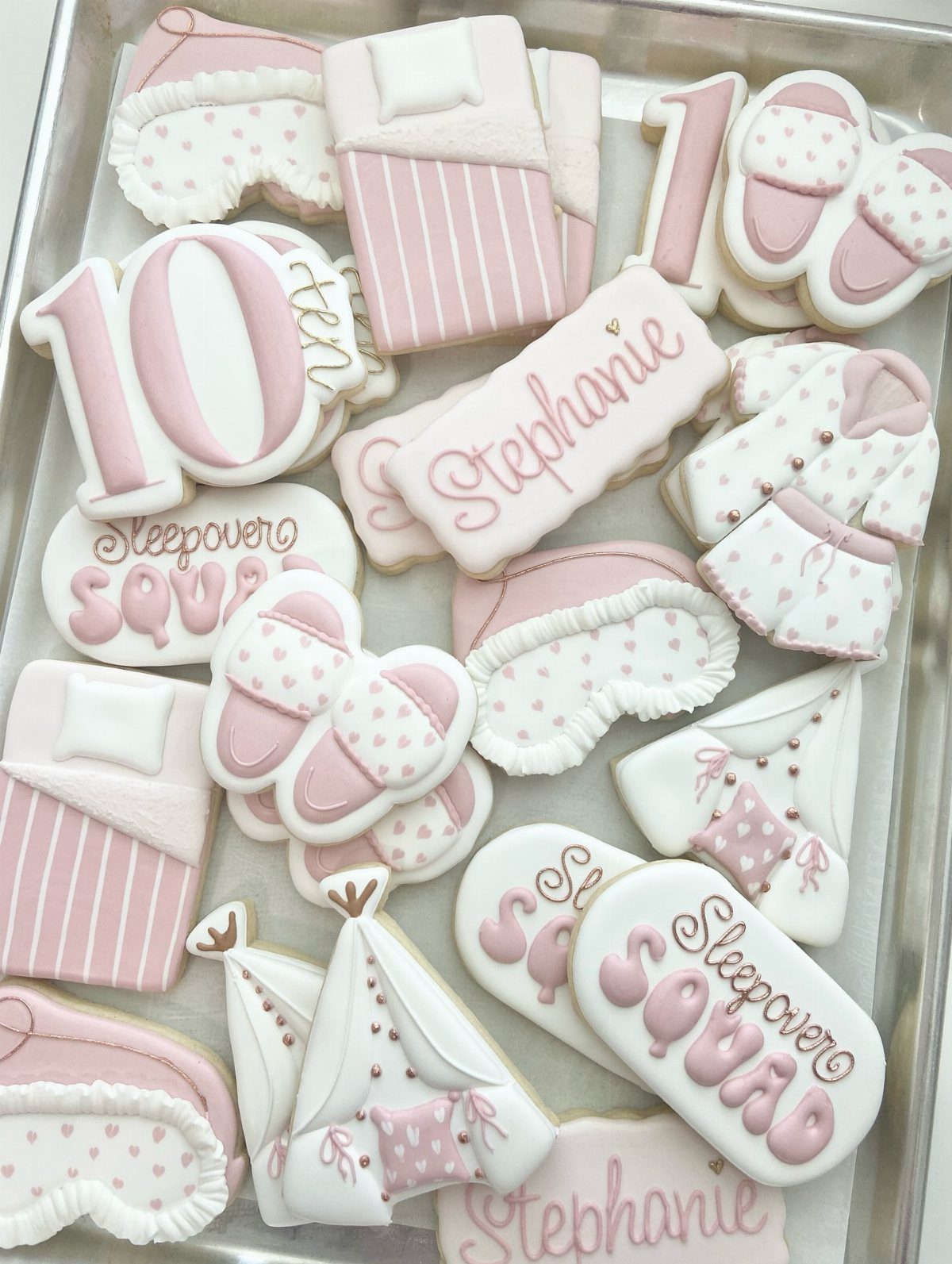 Pink and white decorated sugar cookies in slumber party shapes on a tray.