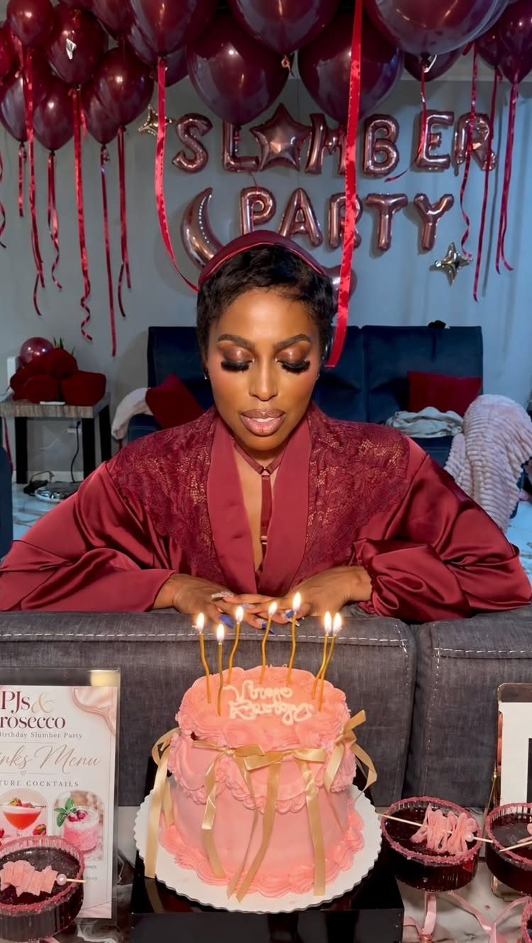 Woman in maroon robe celebrating with a pink cake and slumber party balloons.