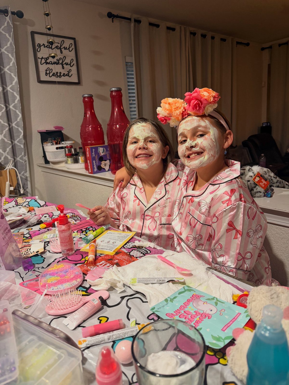 Two girls in pink pajamas wearing white face masks at a spa table.
