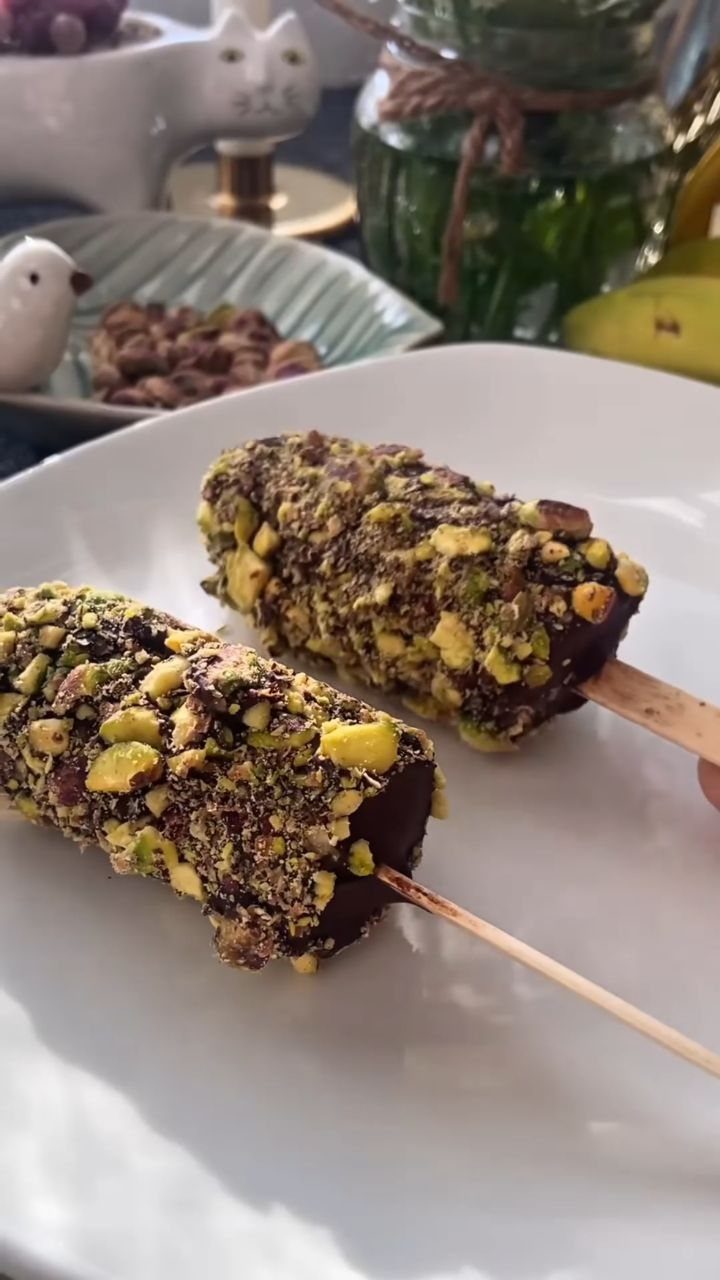 Chocolate-covered banana pops coated in crushed pistachios on a white ceramic plate.