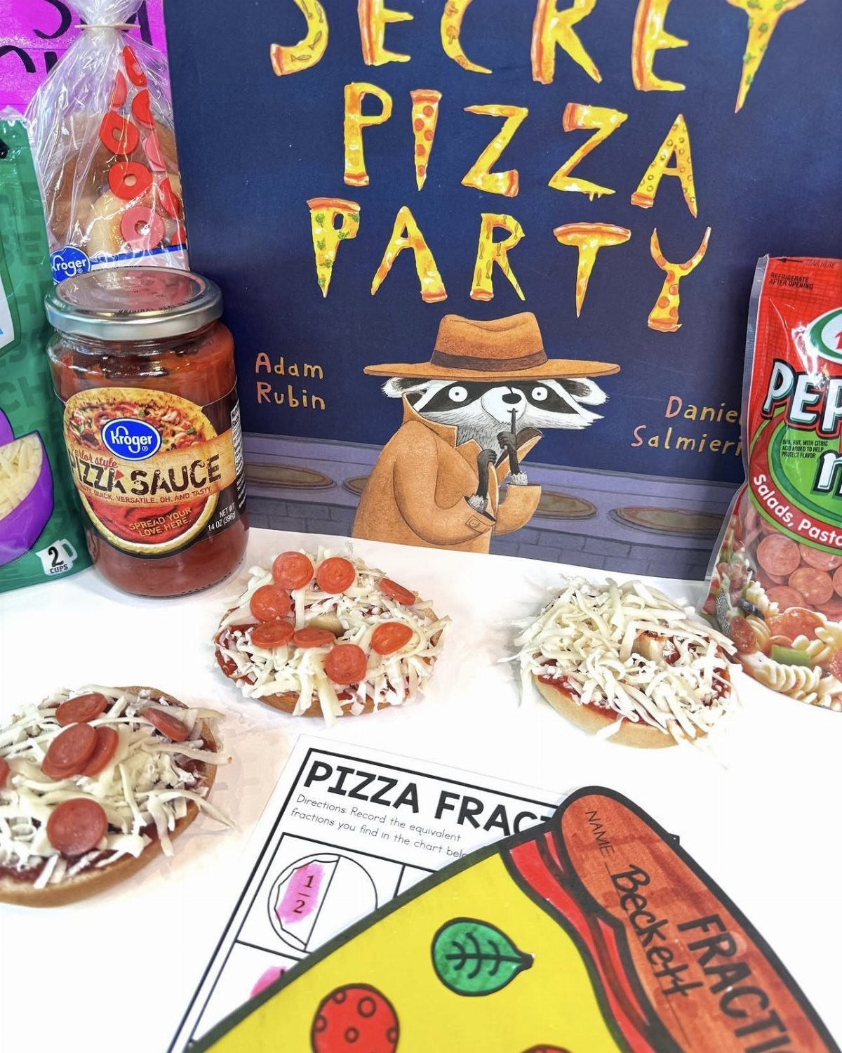 Mini bagel pizzas with pepperoni and cheese next to pizza sauce and book.
