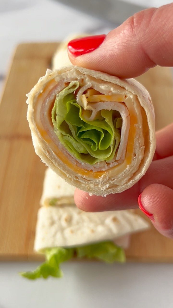 Turkey and cheese tortilla wrap with lettuce held by a hand with red nails.