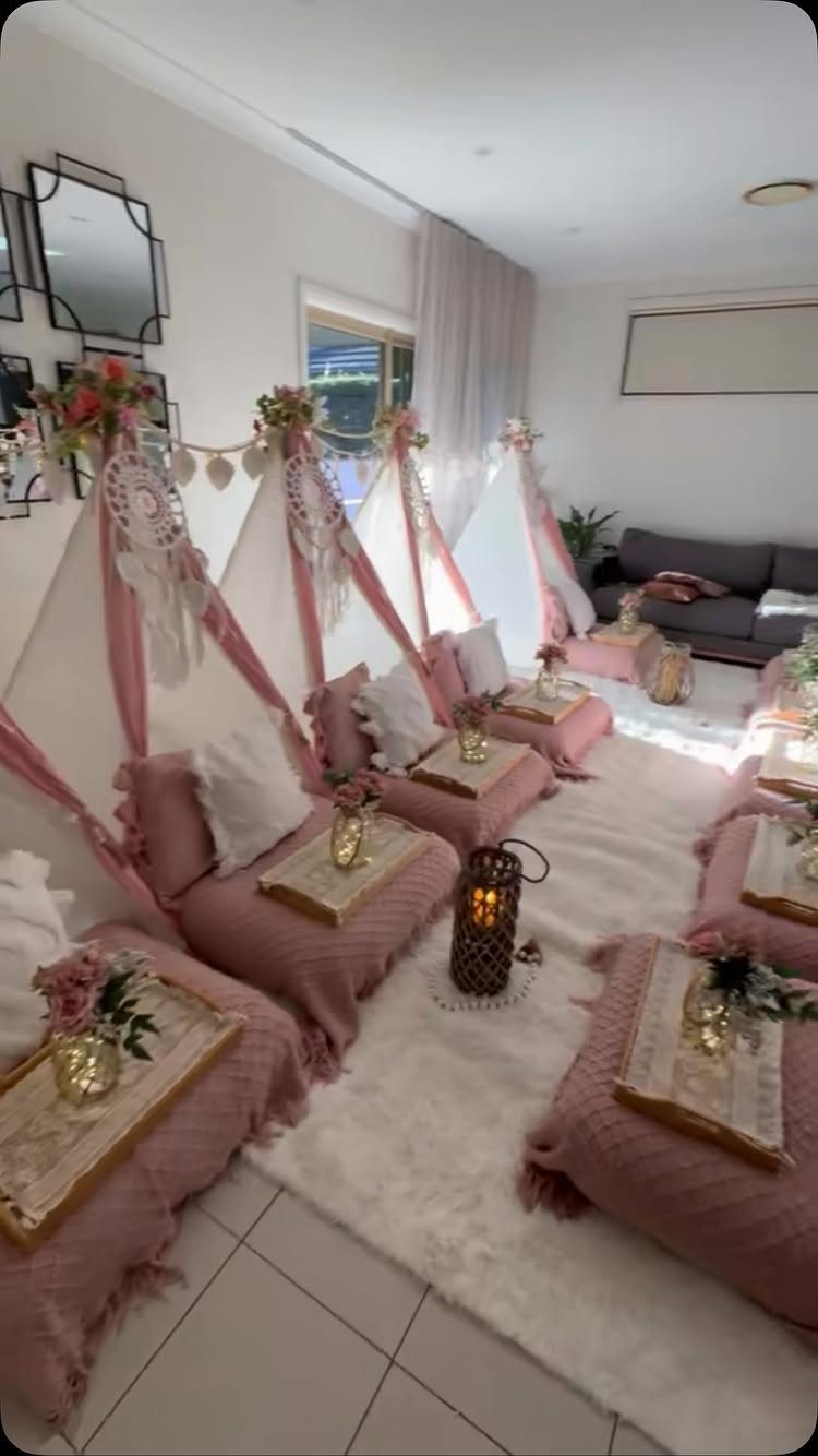 Bohemian teepee tents with pink cushions and gold trays on a white rug.