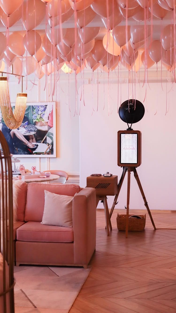 Digital photo booth on a wooden tripod in a room with pink balloons.