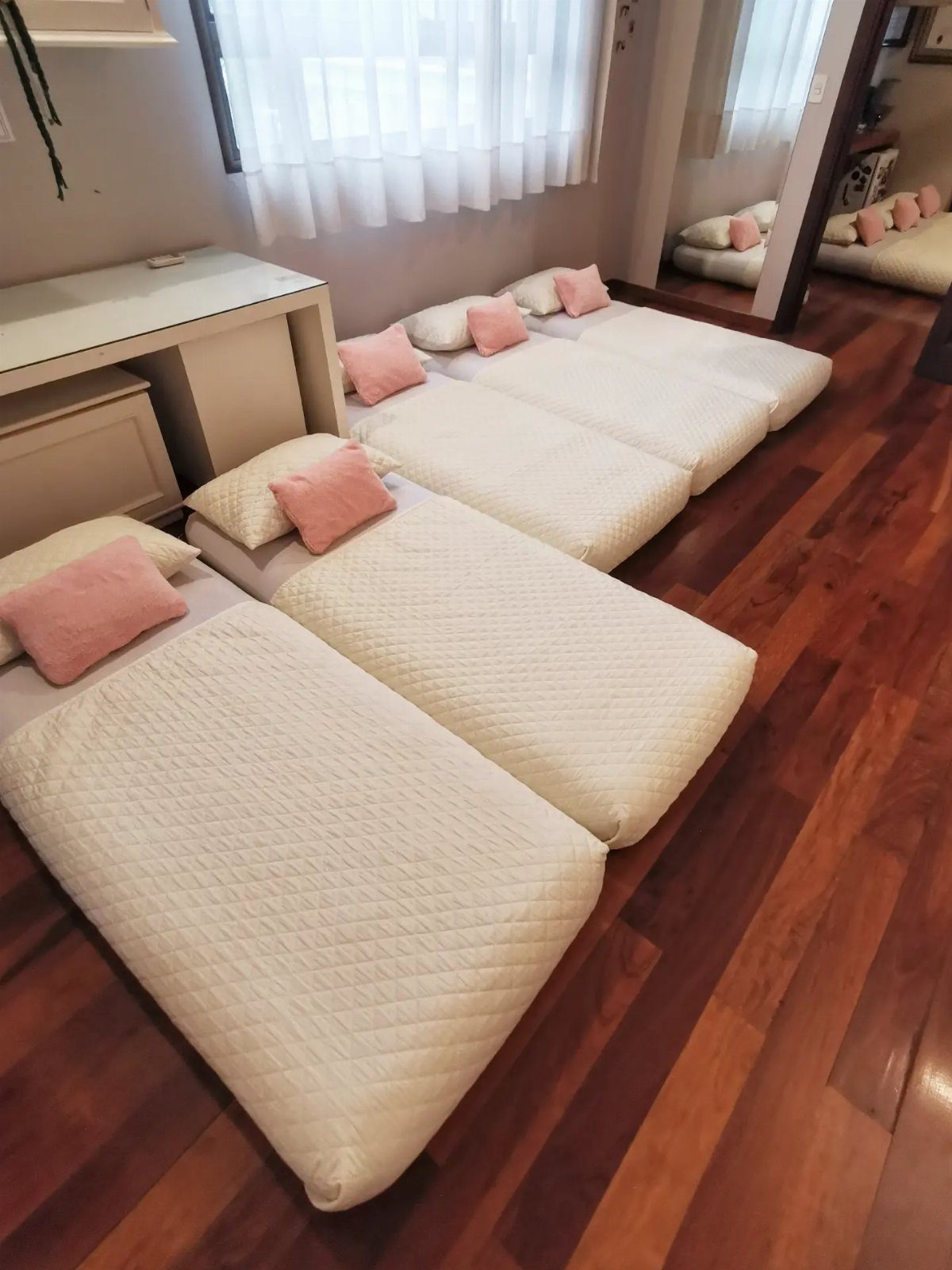 White quilted mattresses with pink pillows arranged on a wooden floor for guests.