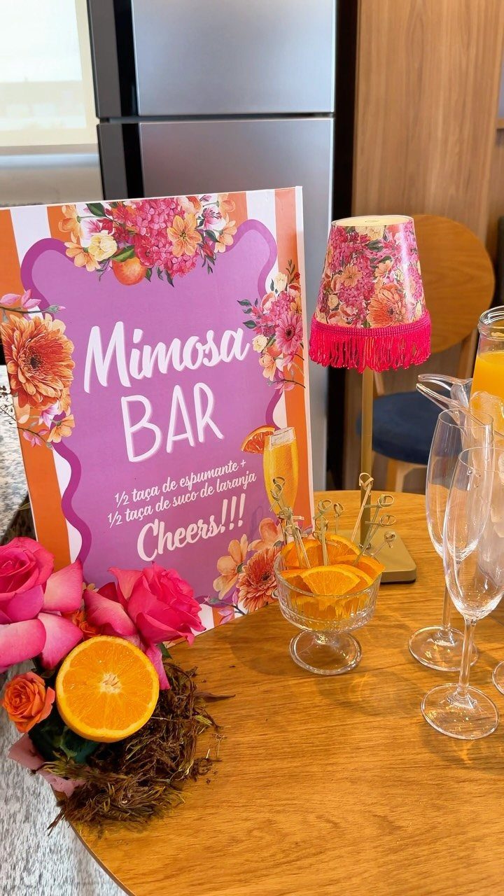 Mimosa bar setup with a floral sign, champagne glasses, and fresh orange slices.