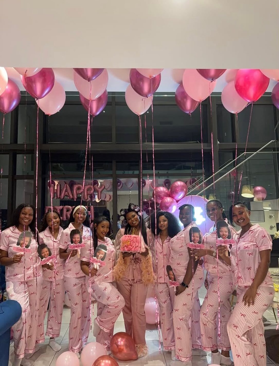 Group of women in pink striped pajamas posing with pink balloons in a room.