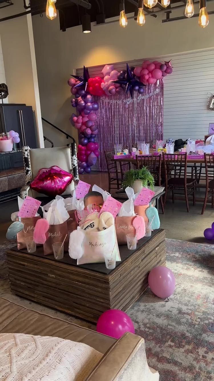 Party setup with pink balloons, gift bags on a table, and tinsel backdrop.
