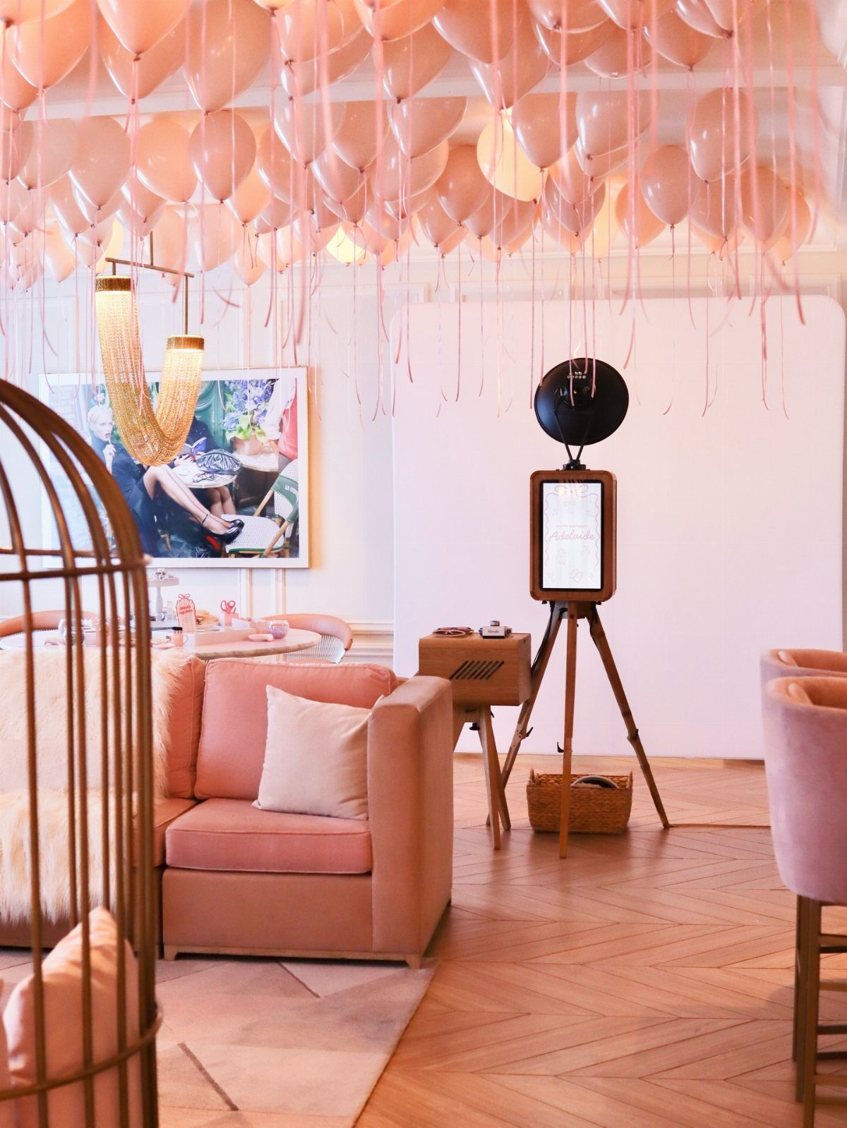 Peach balloons on a ceiling above a pink sofa and photo booth setup.