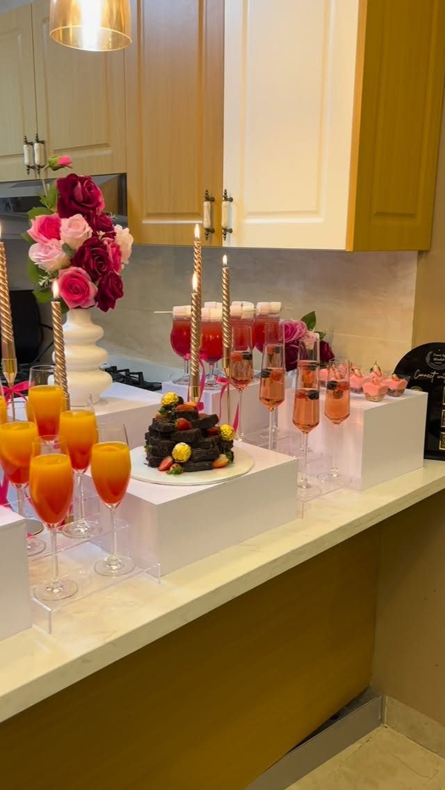 Cocktails, a chocolate cake, and pink roses arranged on a white kitchen counter.