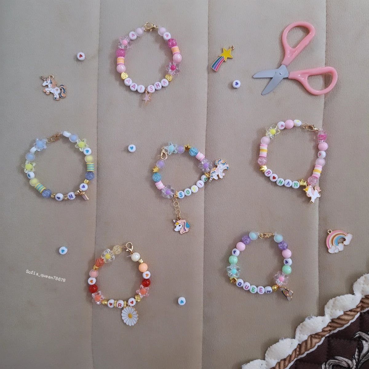 Colorful beaded friendship bracelets with charms and pink scissors on beige fabric.