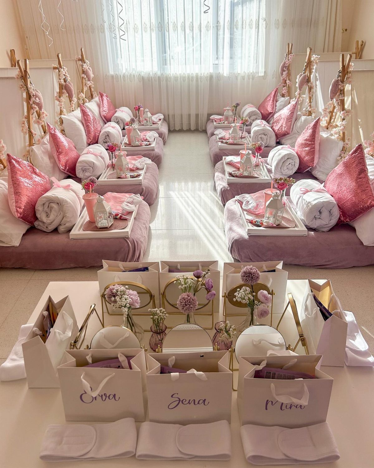 Pink and white floor mattresses with pillows and gift bags for a party.