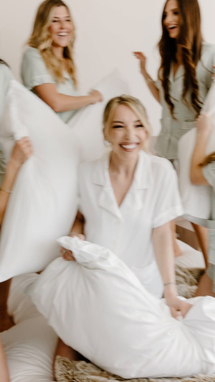 Women in pajamas laughing and holding large white pillows for a pillow fight.