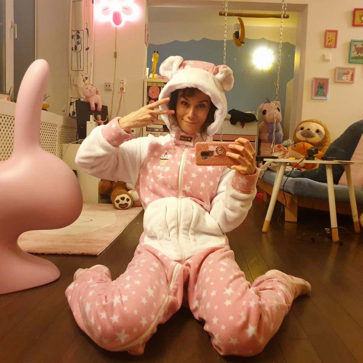 Woman in a pink star-patterned animal onesie taking a mirror selfie in a bedroom.