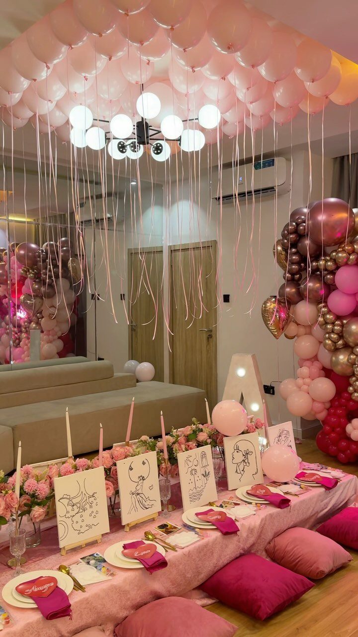 Pink party setup with low table, floor cushions, and ceiling balloons.