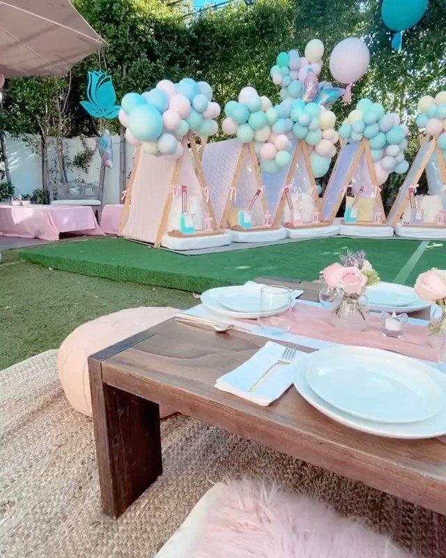 Outdoor slumber party setup with pastel balloons, teepees, and a low wooden table.