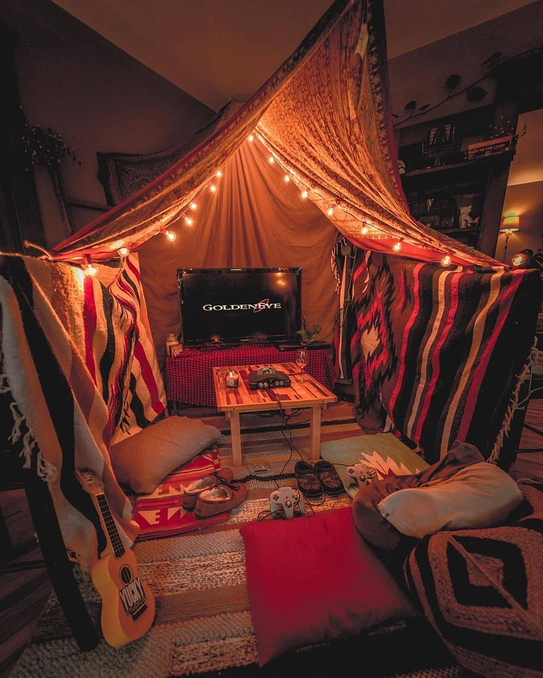 Cozy indoor blanket fort with string lights, pillows, and a television screen.