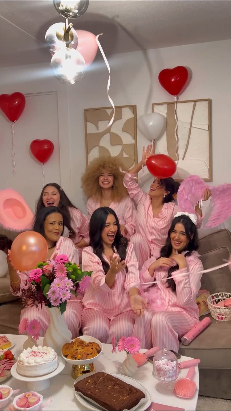 Six women in matching pink striped pajamas posing with heart balloons and party food.