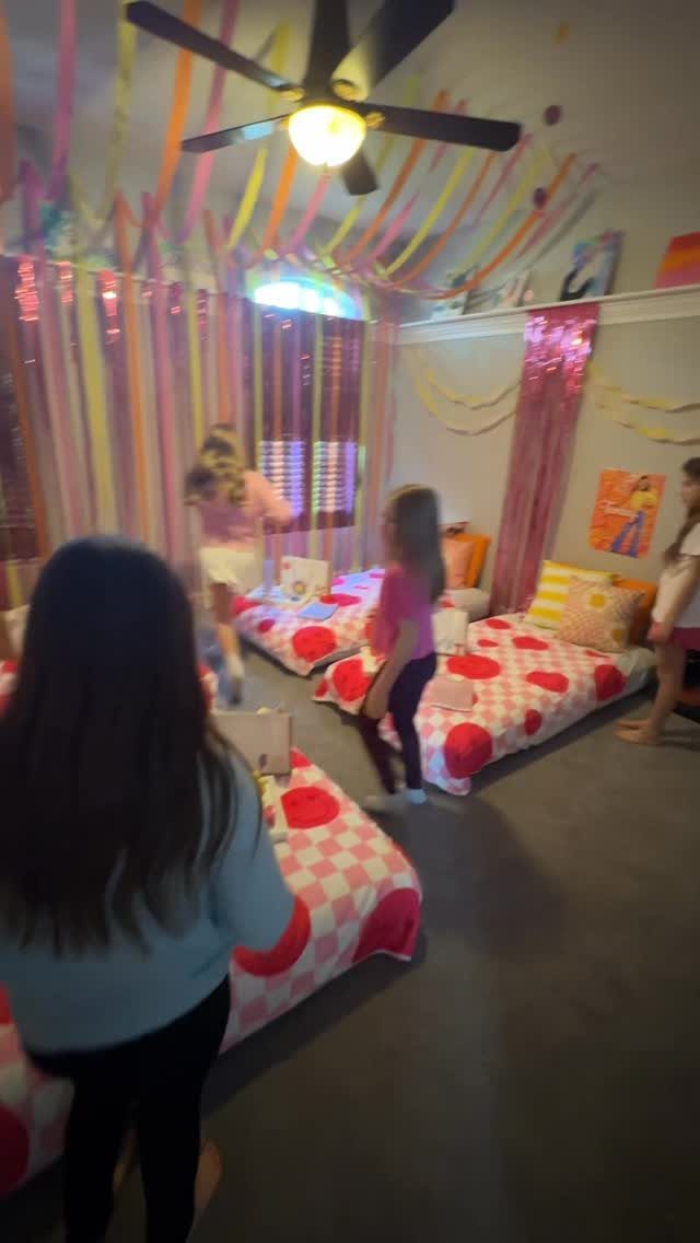 Girls in a room with colorful streamers and polka-dot bedding for a slumber party.
