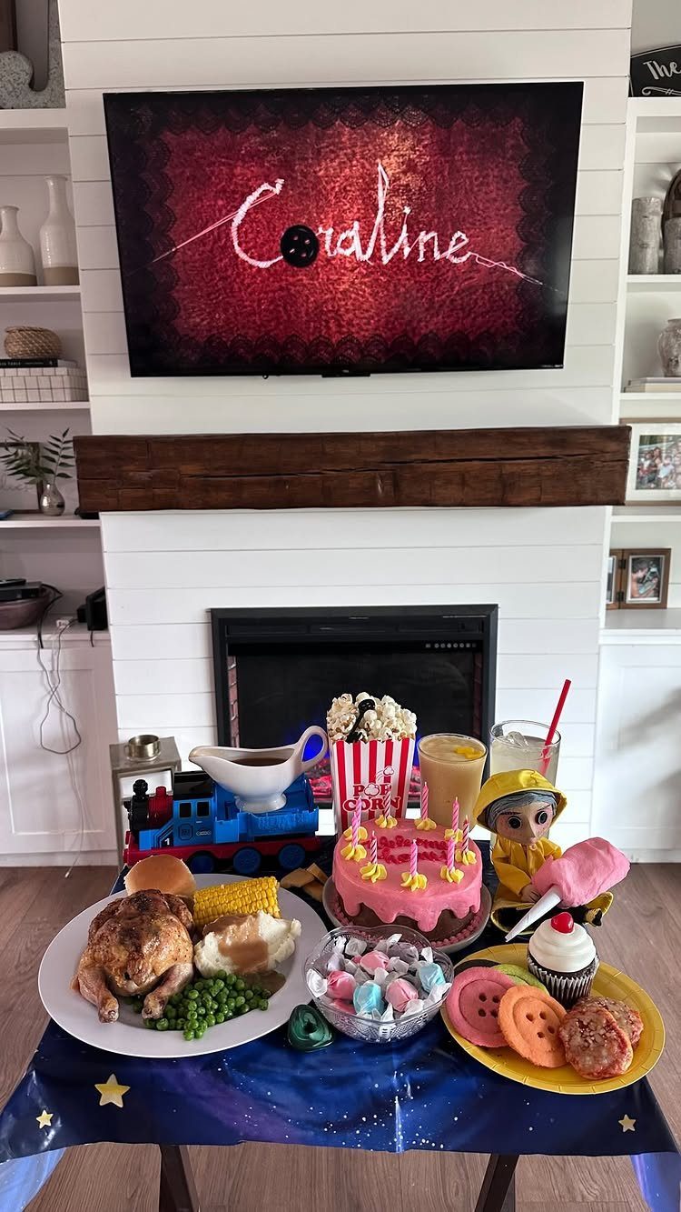 Themed dinner spread with roasted chicken and cake under a Coraline movie screen.