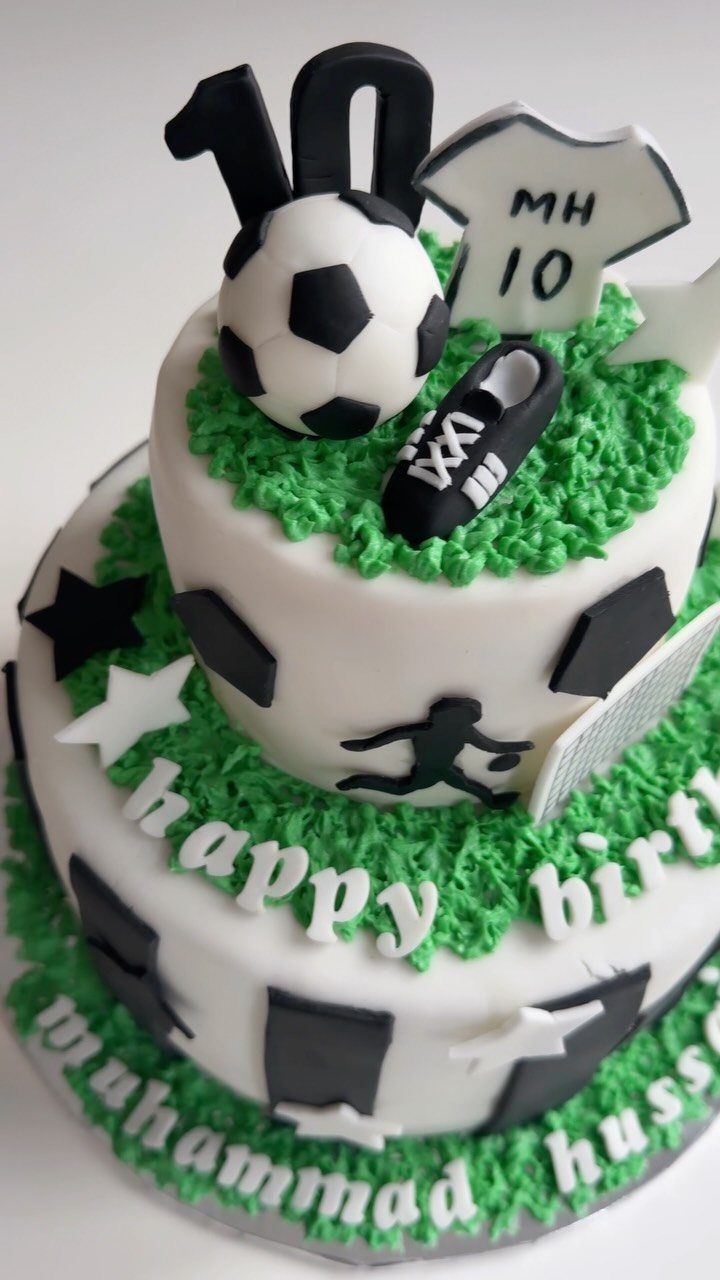 Two-tier white soccer cake with green grass, a soccer ball, and birthday lettering.