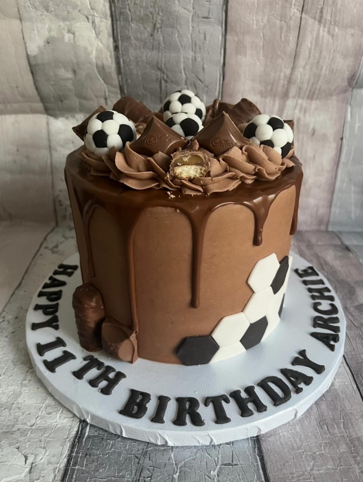 Chocolate drip birthday cake decorated with soccer balls and birthday text for Archie.