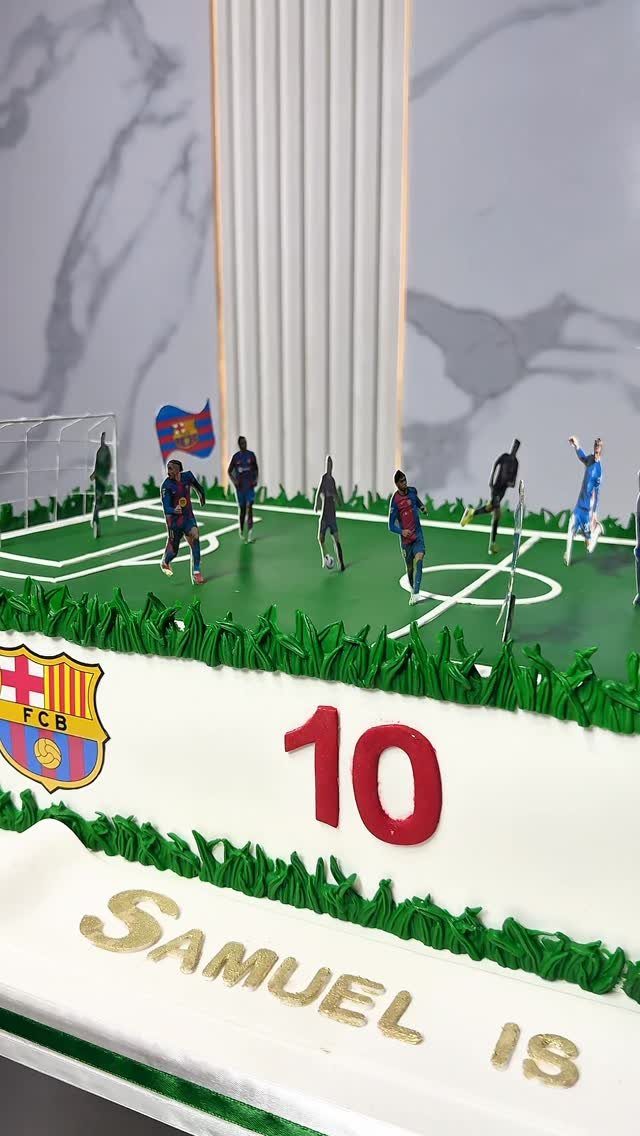 Soccer themed birthday cake with miniature players on a green field and FC Barcelona logo.