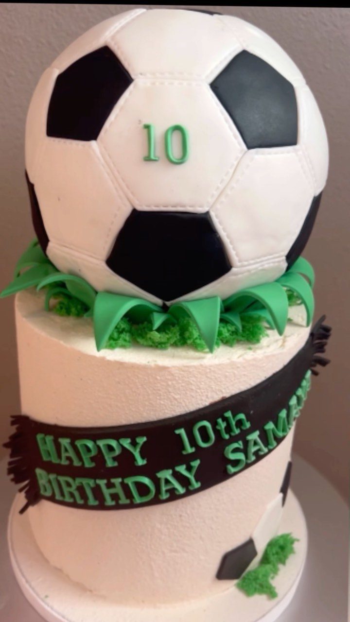 Two-tier soccer birthday cake with a 3D soccer ball on top and green grass.