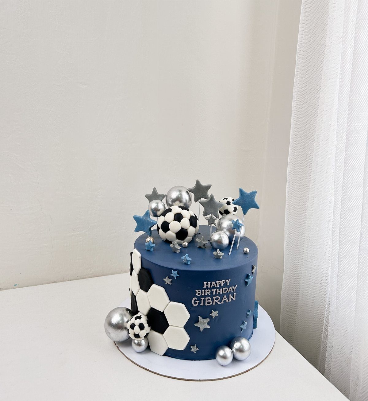 Blue soccer themed birthday cake with white lettering and soccer ball decorations.