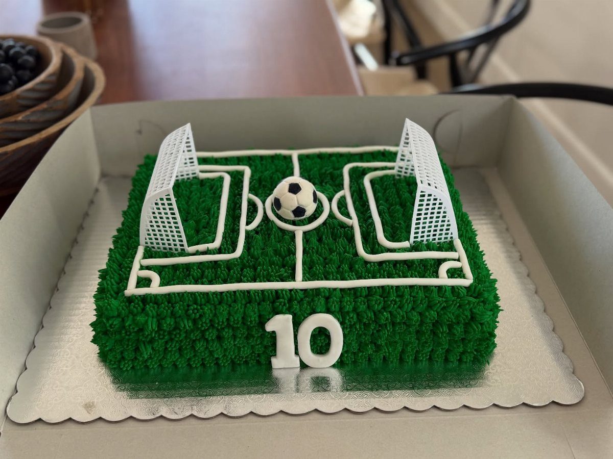 Soccer field cake with green frosting, white goals, and a soccer ball topper.