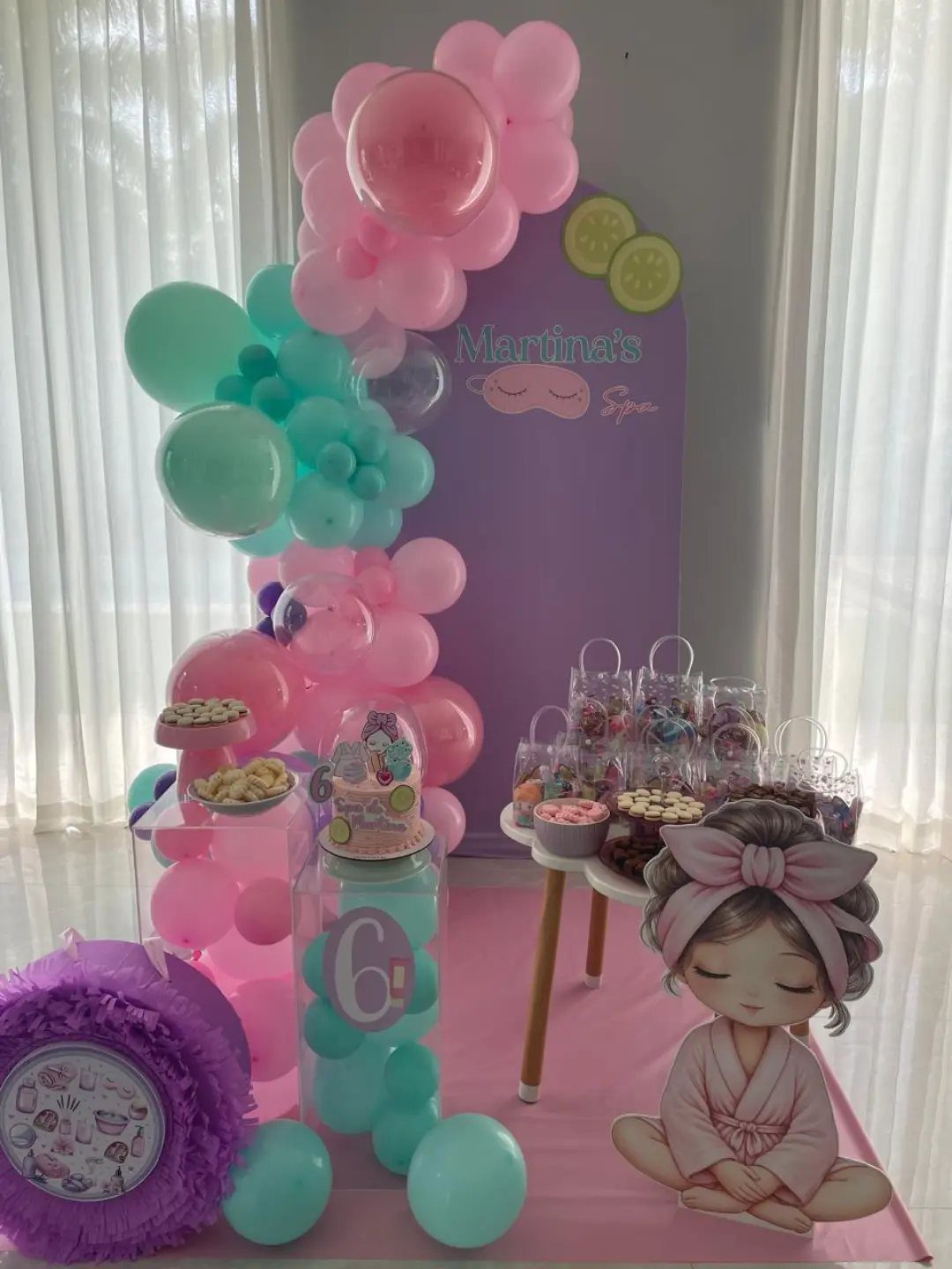 Pink and teal balloon garland arching over a purple spa party backdrop