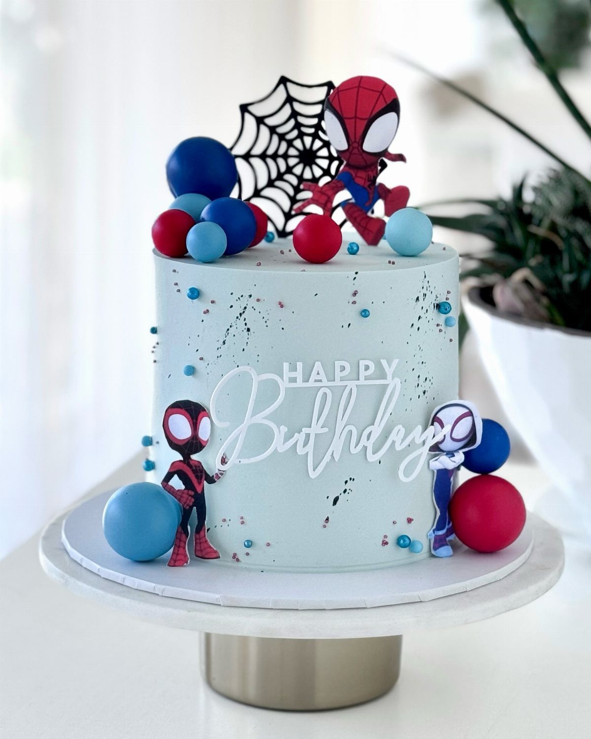 Light blue birthday cake decorated with baby Spider-Man figures and colorful spheres.