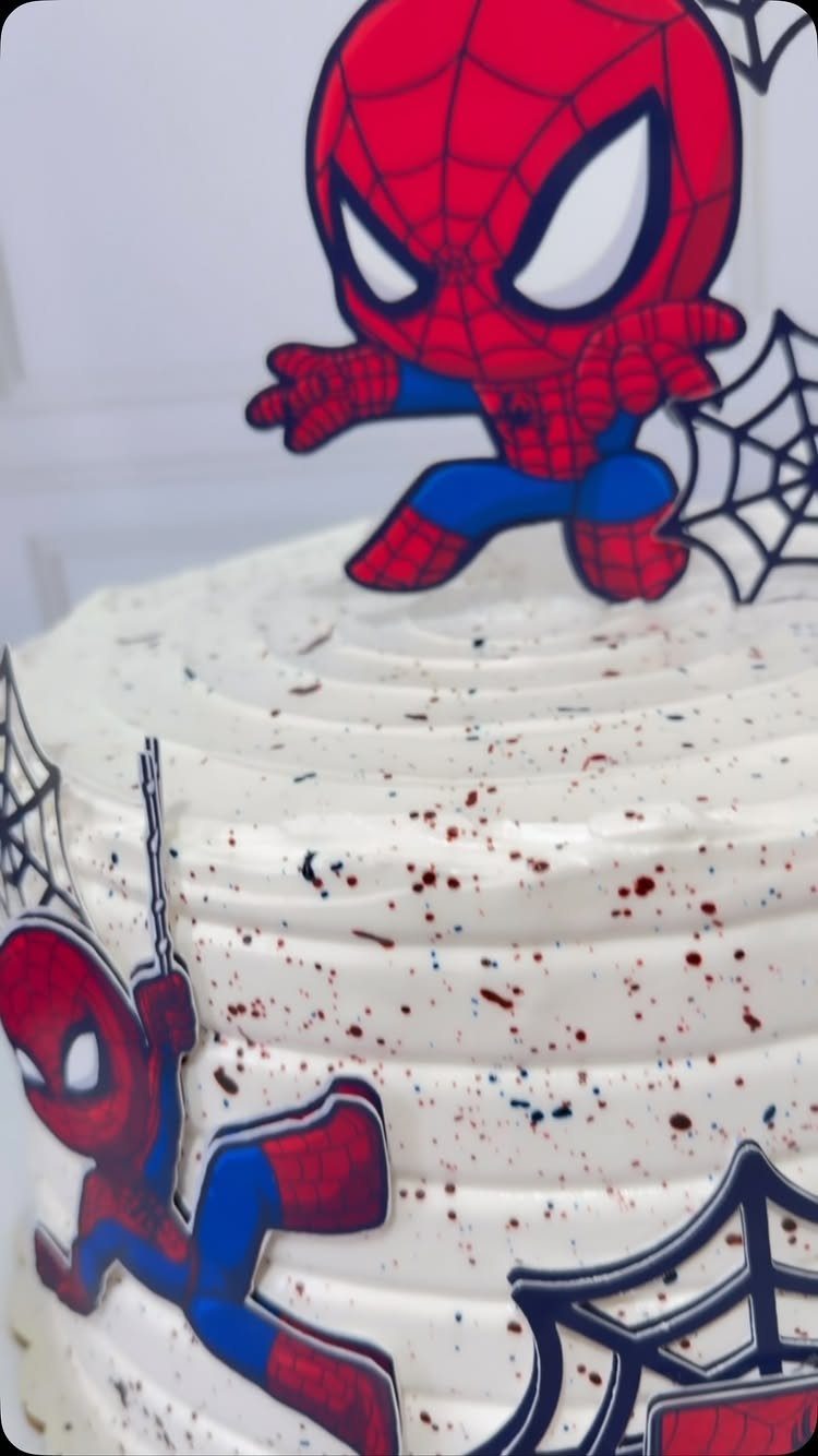 White frosted cake with red and blue splatters and Spider-Man character toppers.
