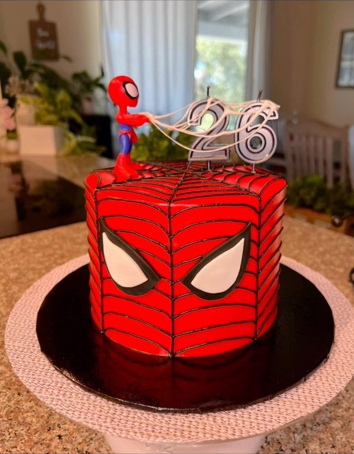 Spider-Man mask cake with a small figurine and silver number 26 candles.