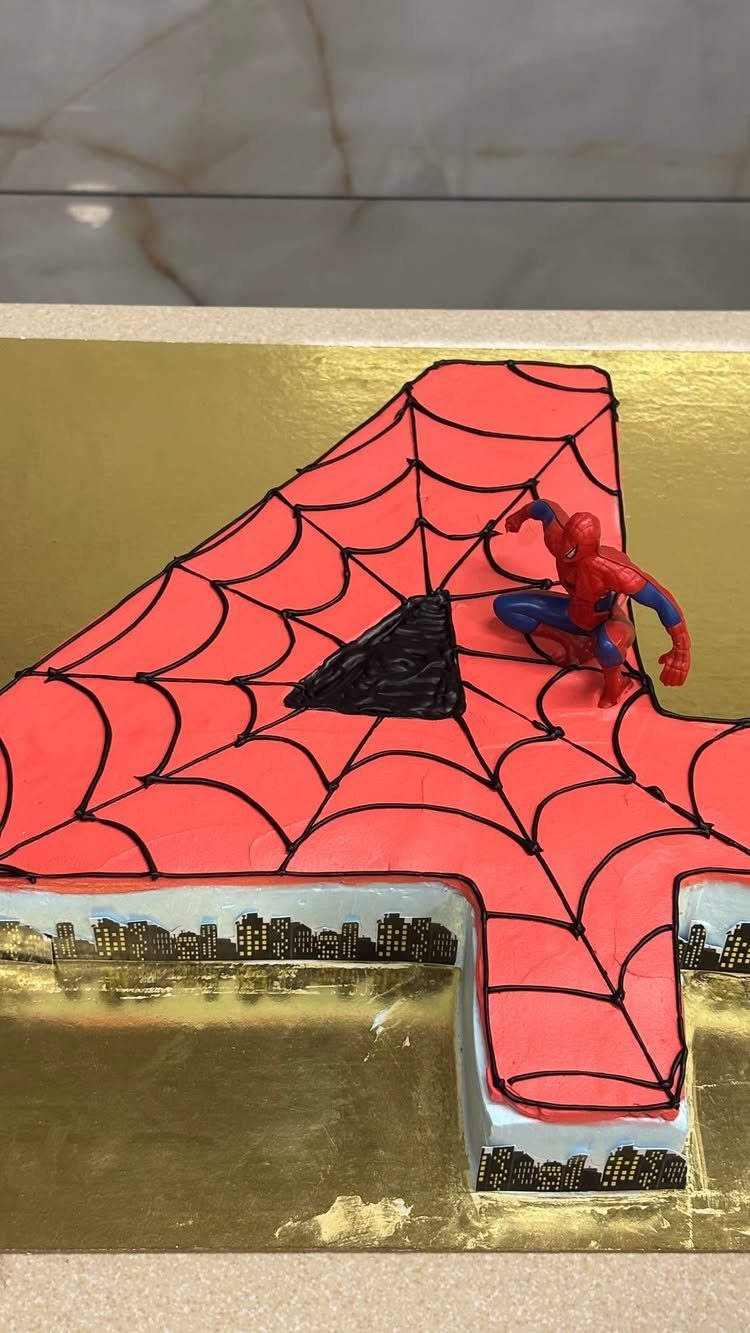 Number four shaped red cake with black webs and a Spider-Man figurine.
