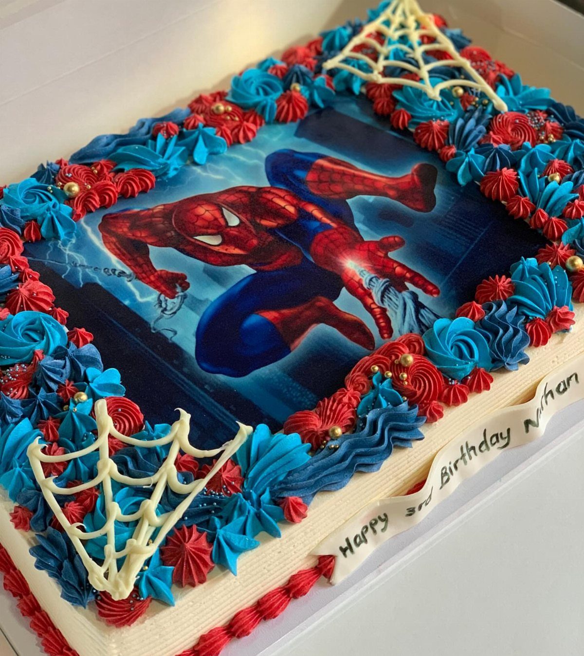 Rectangular sheet cake with Spider-Man edible image, red and blue frosting, and webs.