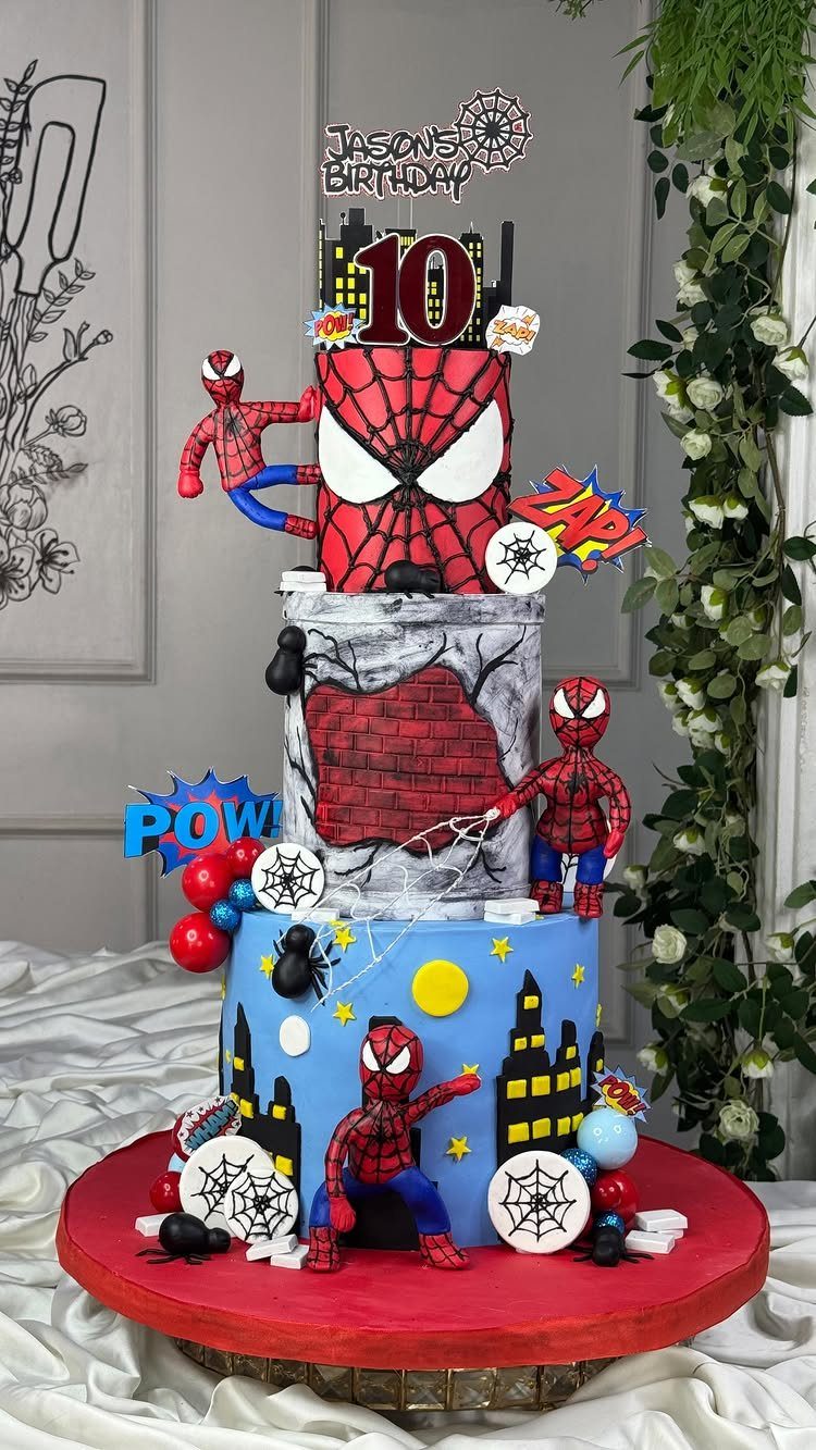 Three-tiered Spider-Man cake with city skyline, brick wall, and character figurines.