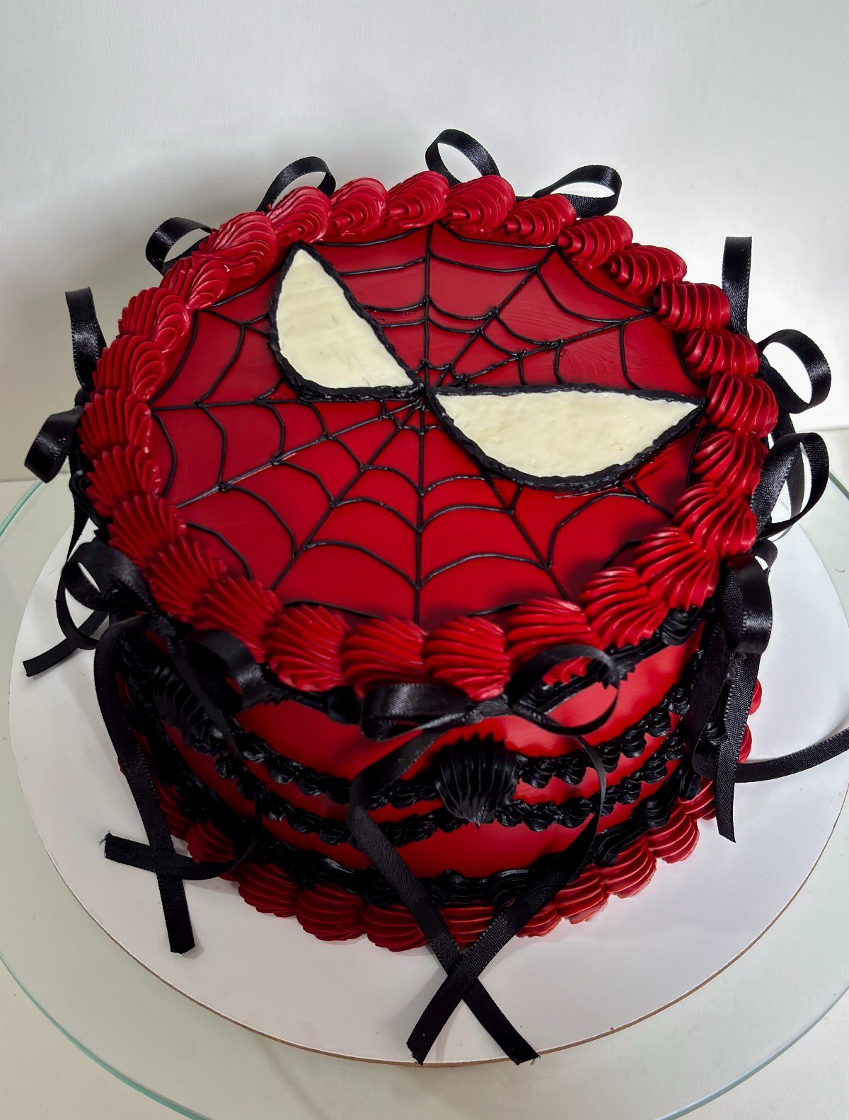 Spider-Man themed birthday cake with red frosting, black webbing, and black ribbon bows.
