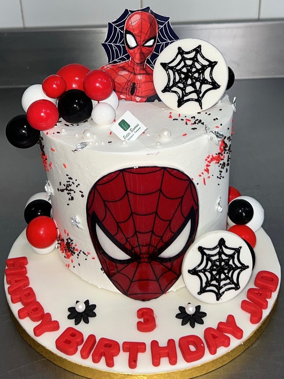 White Spider-Man birthday cake with red lettering, web discs, and colorful candy toppers.