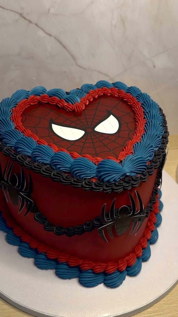 Heart-shaped Spiderman cake with red frosting, black spiders, and blue piped borders.
